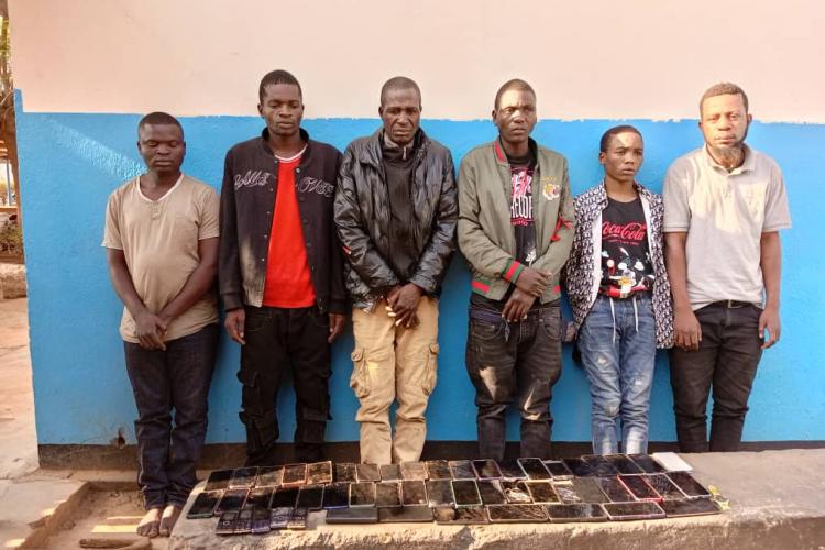 Suspects in handcuffs posing with the stolen phones